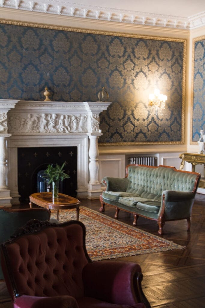 Orante cloth wallpaper with gold accents and a white fireplace in a living room of a castle