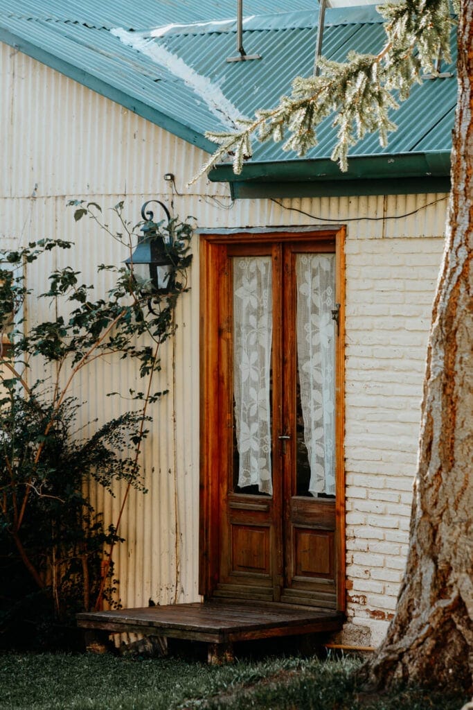 A building of yellow corregated tin wall with a wooden door and ivy growing up its side