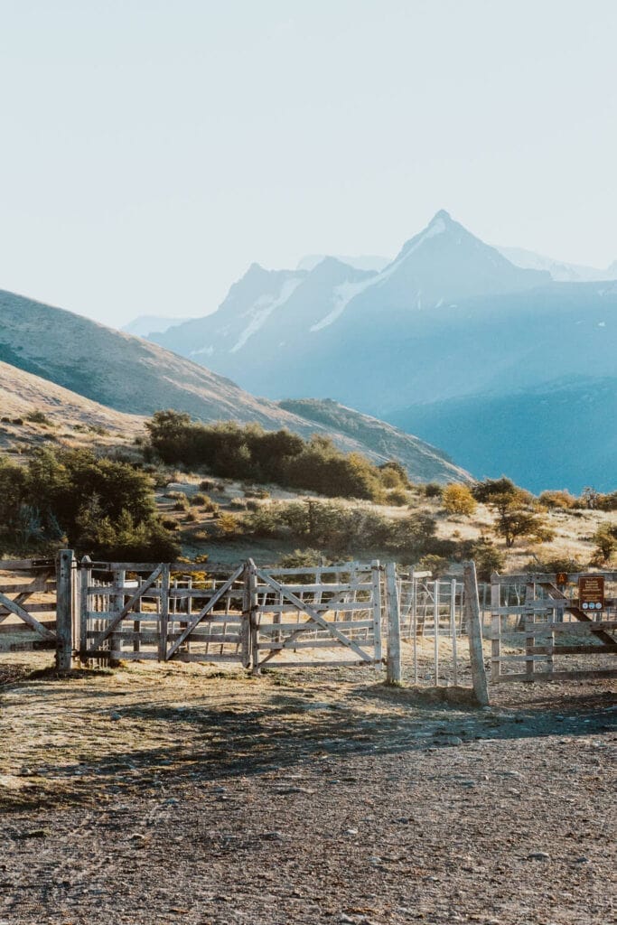 A grouping of fences and a dirt road sit in front of pastures and mountains