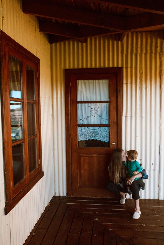 A woman holds a baby on her knee as she crouches in front of a wooden door