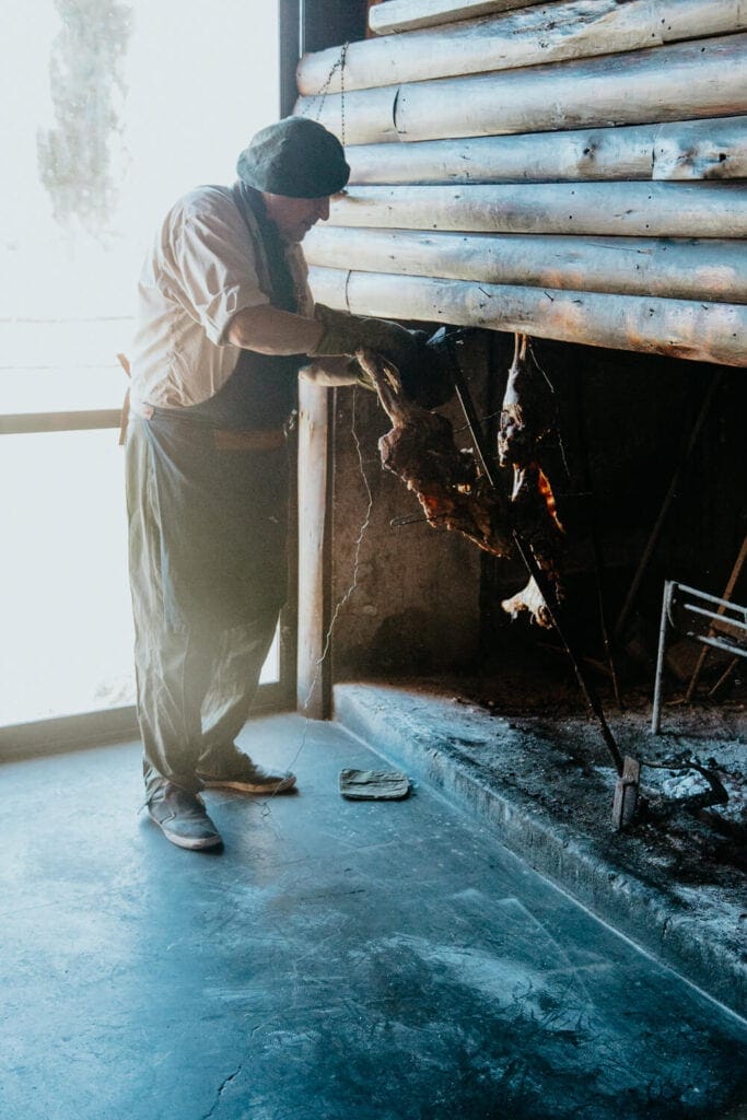 A man stands next to a lamb on a spit over open fire