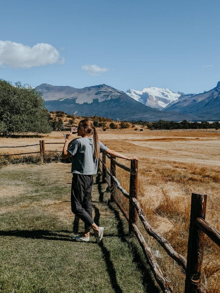 A woman stands next to a fence with a glass of wine in her hand pretending to take a drink for the photo
