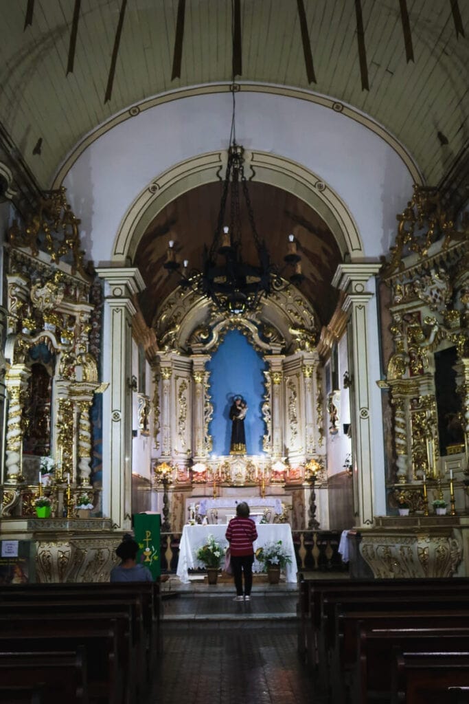 A woman stands at the alter of a golden alter of a historic church