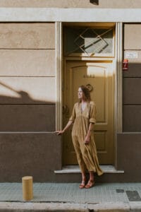 A woman in a yellow dress stands in front of a beige wall and yellow door