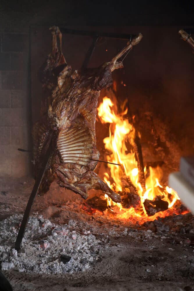 A rack of lamb roasts over an open fire on a metal cross.