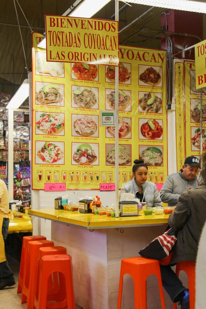 Red plastic stools at a yellow bar serving tacos in Mexico City