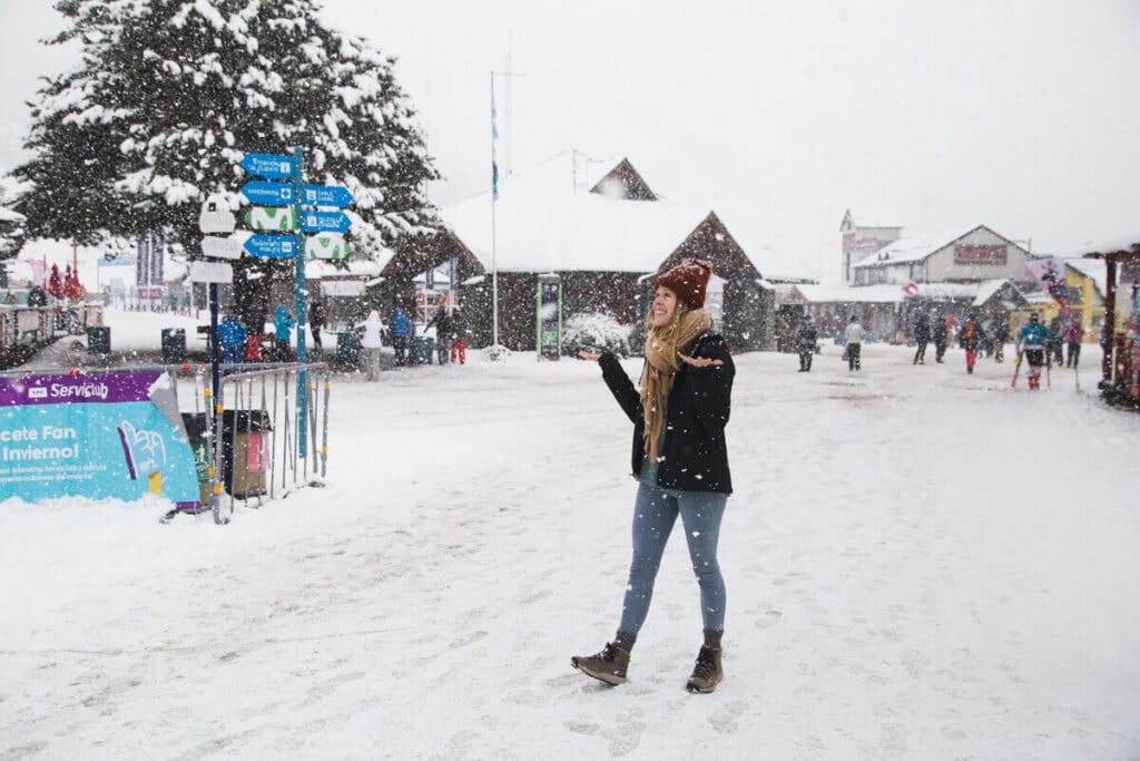 A woman stands in the snow with her hands up catching snowflakes