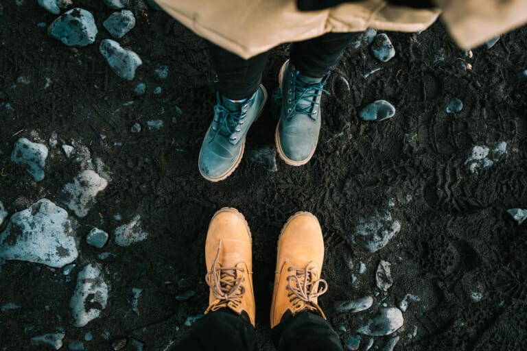 Two pairs of shoes on a black beach seen from above