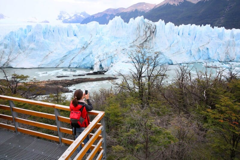 A woman takes a picture of a glacier with her phone