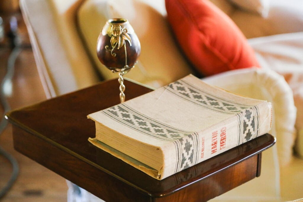 A book and mate cup on a side table by a sofa