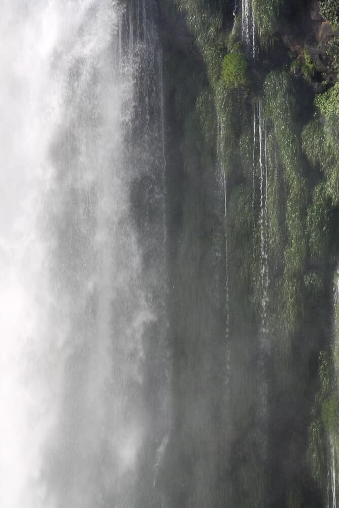 A waterfall in front of a moss covered wall