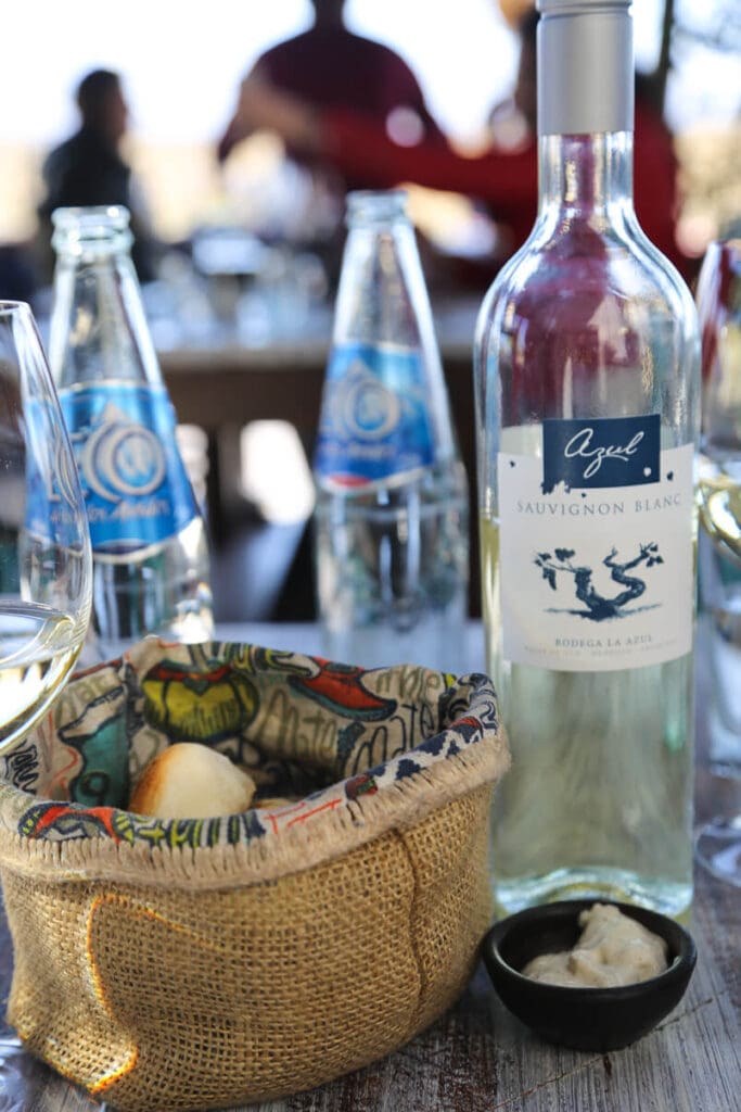 A bottle of white wine on a table by a bread basket