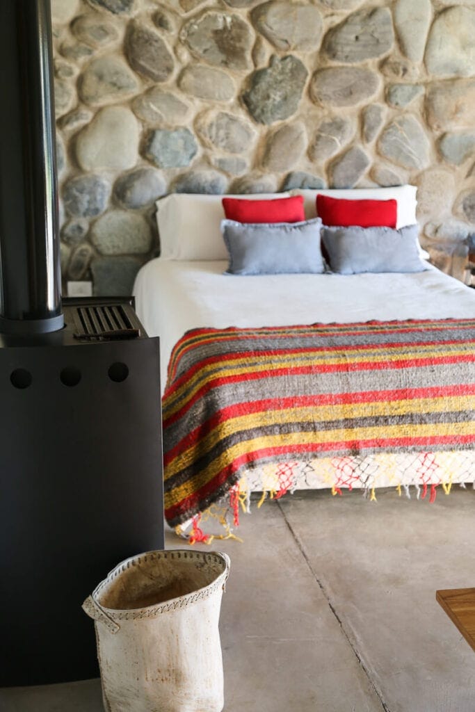 A bed with a quilt in front of a wall of river stones