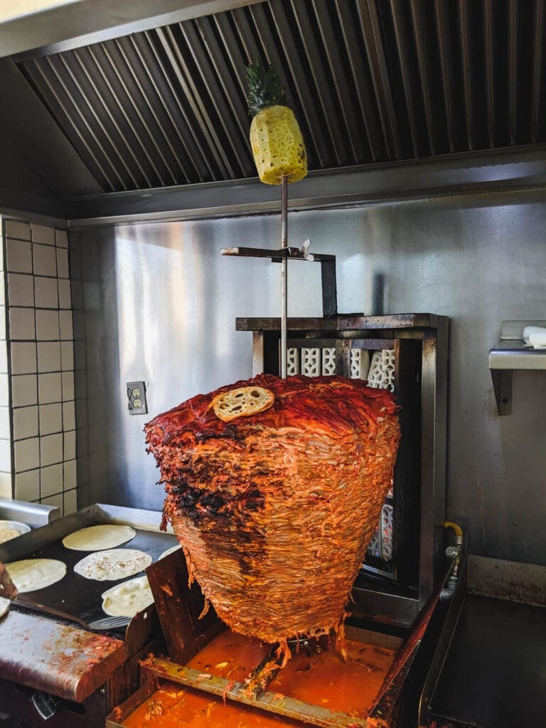 A large spit of meat with a pineapple on top