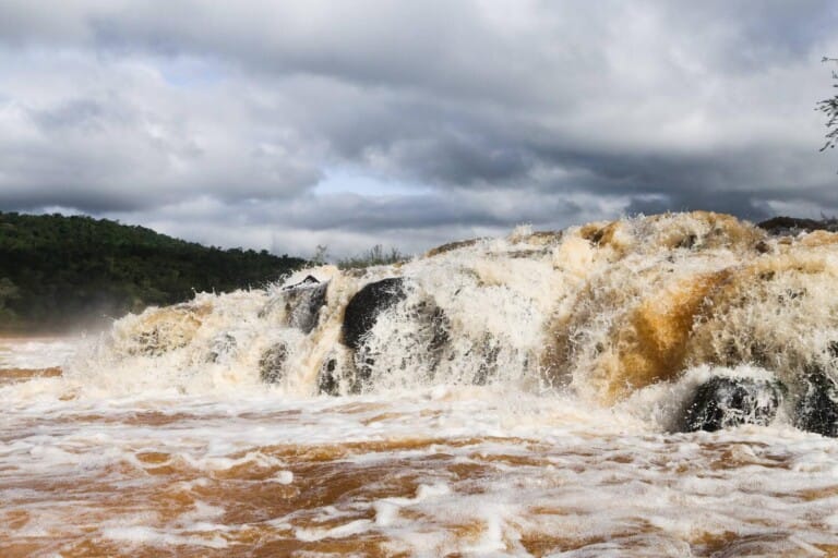 Water pours into a brown river from a short waterfall