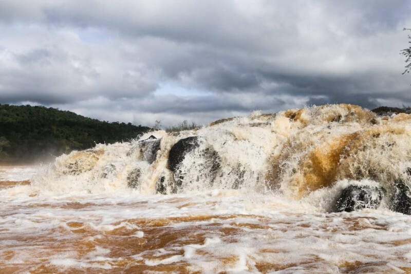 Water pours into a brown river from a short waterfall