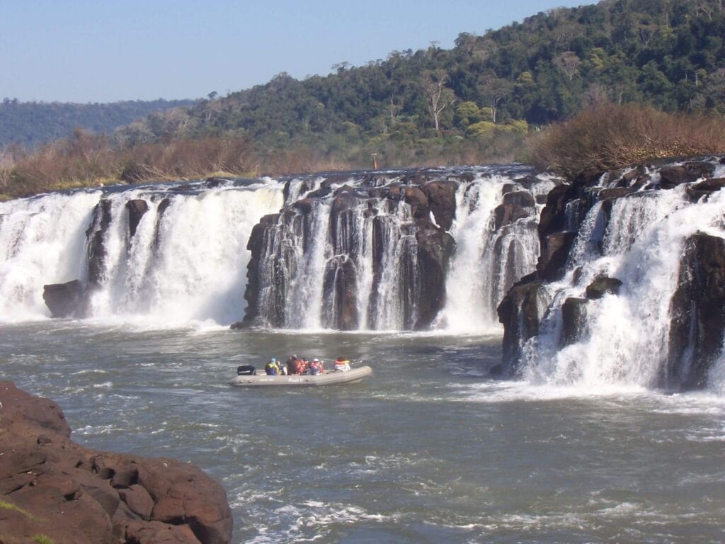 A small speed boat in the water below waterfalls