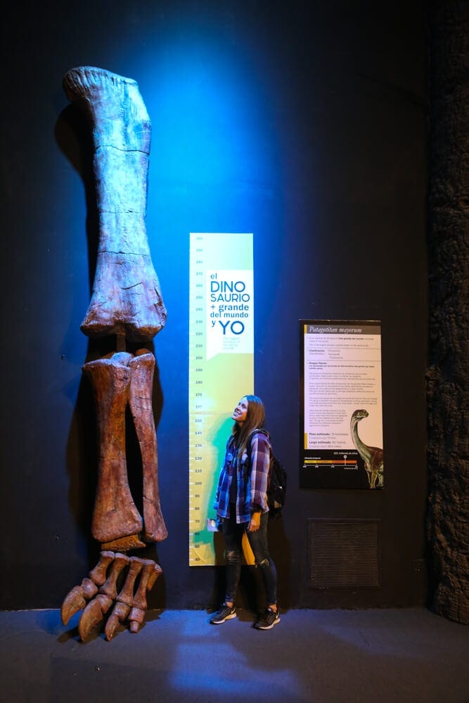 A woman stands next to a statue of a dinosaur leg