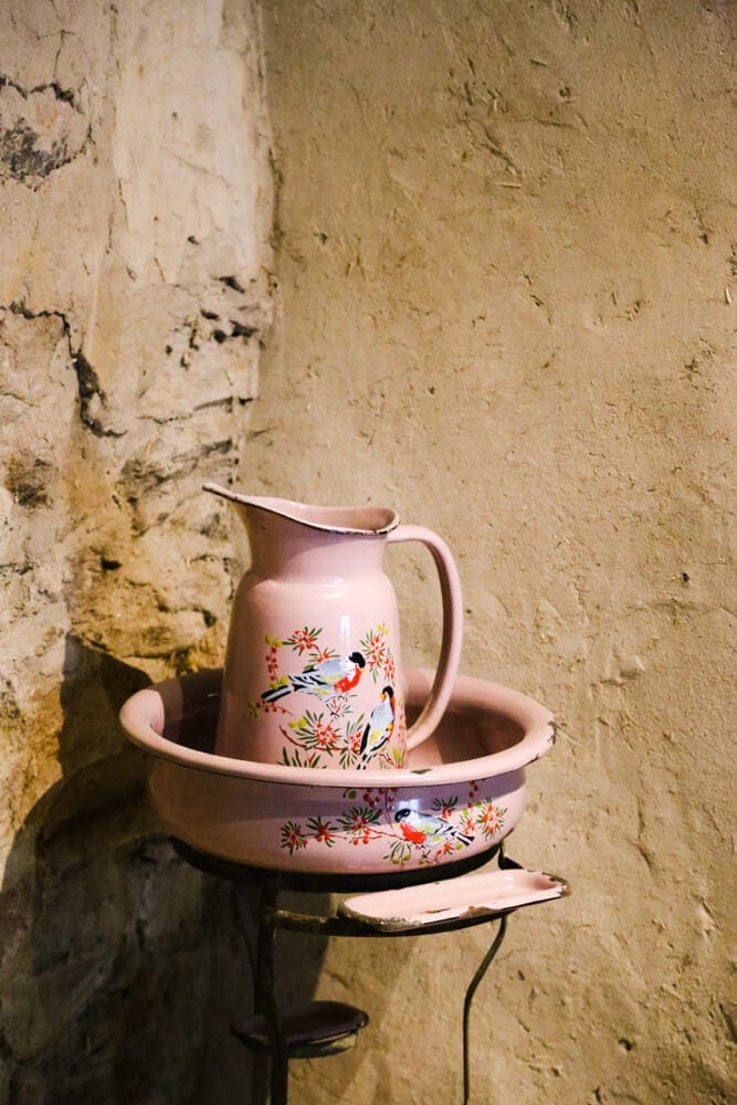 A metal pink jug of water by a stone wall