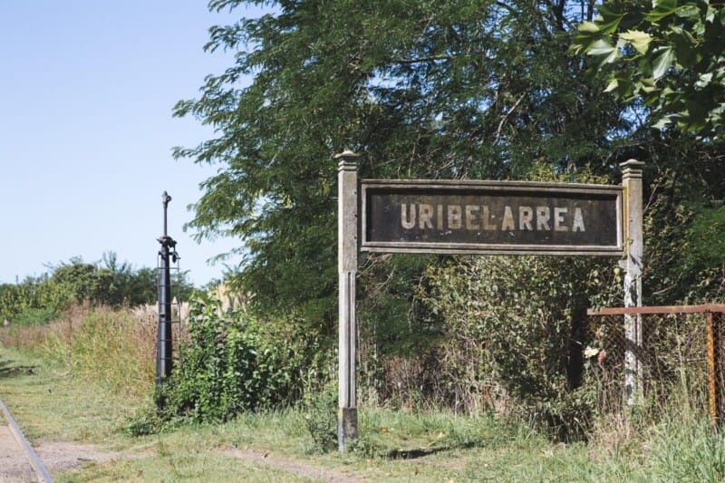 An aged city sign in the grass next to train tracks