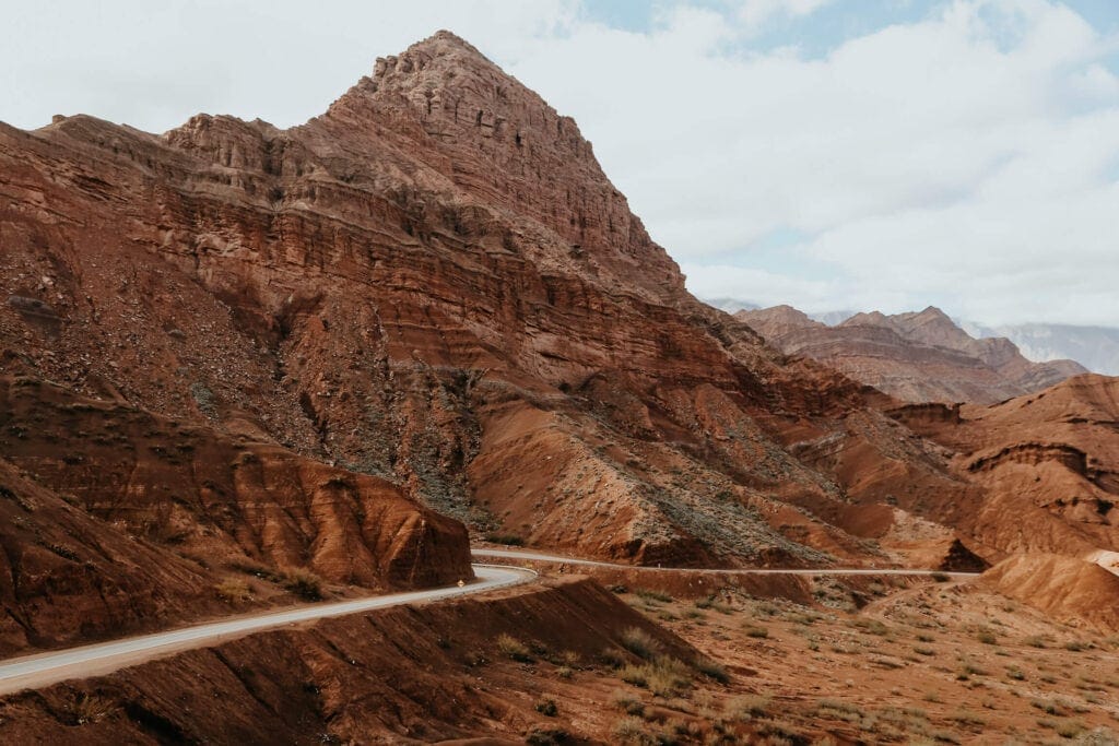 A highway weaves along next to a red mountain in the desert