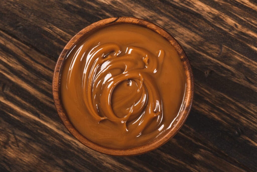 A bowl of creamy dulce de leche on a wooden table