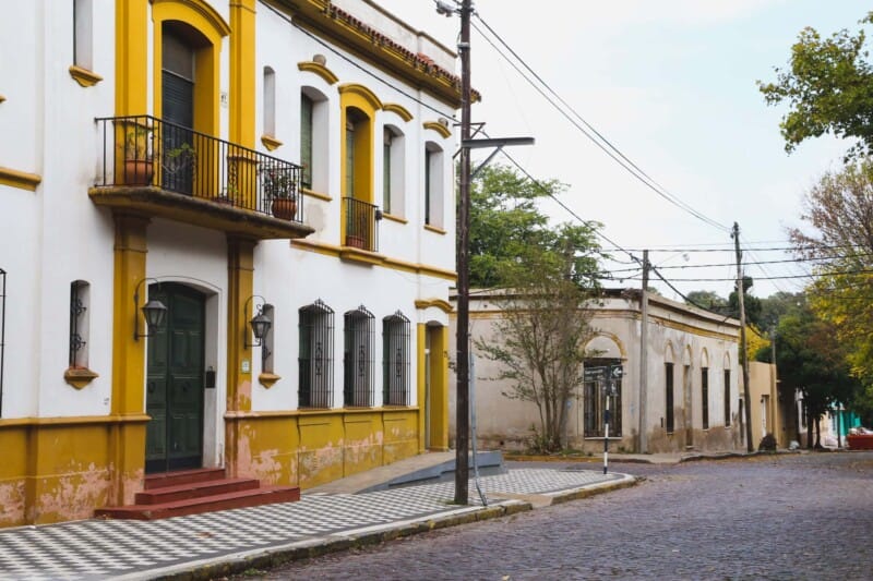 A yellow and white building with a green door next to a checkerboard sidewalk and cobblestone street