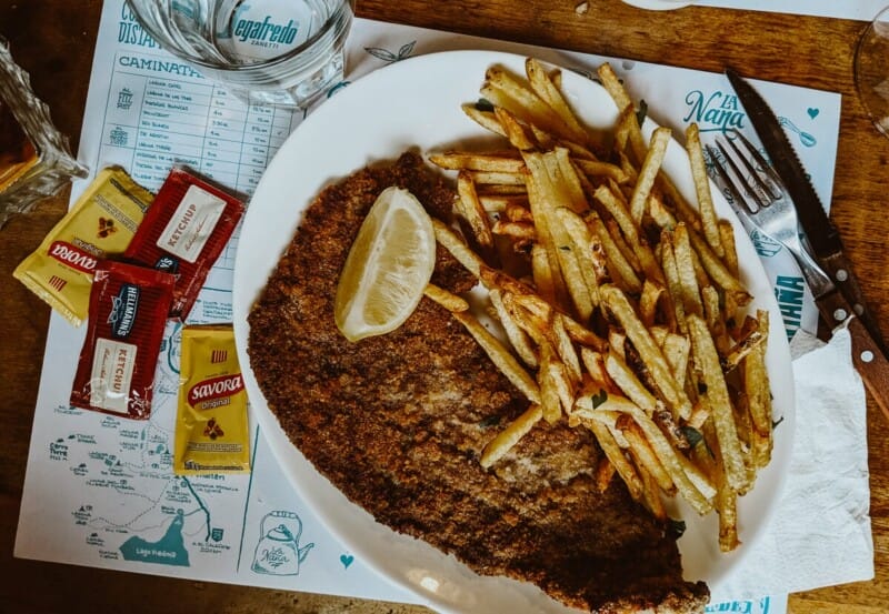A breaded schnitzel and french fries on a plate with ketchup packets