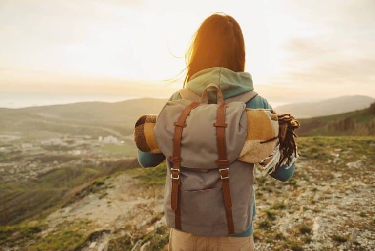 A woman with a backpack on in the countryside has her back to the camera