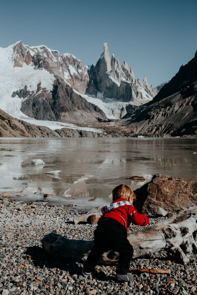 A baby crawls on a rocky beach at a mountain lake