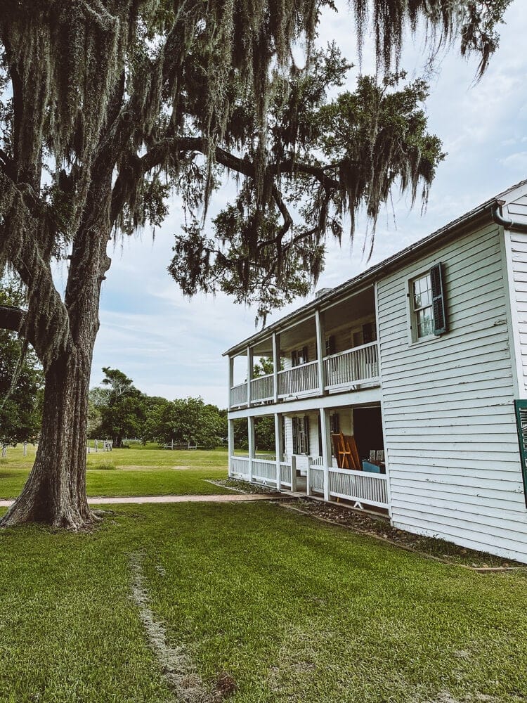 A two story white wooden inn under an oak tree covered in Spanish moss