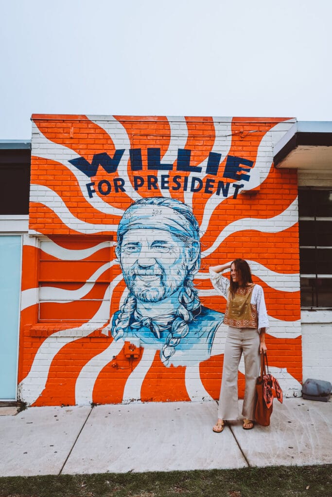 A woman stands in front of a red and white mural of willie nelson