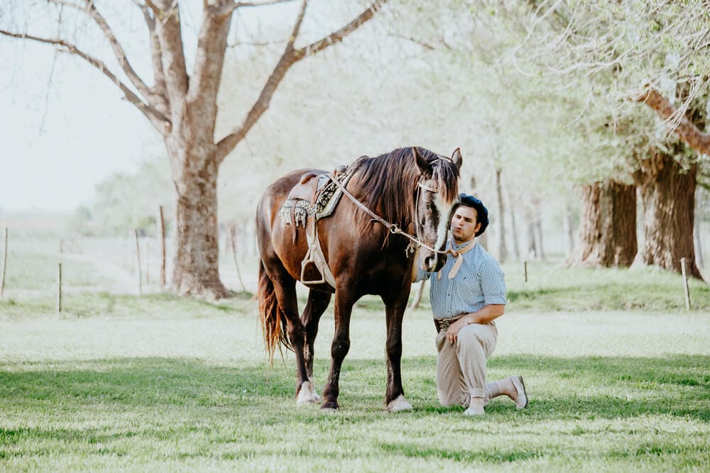 An Argentine gaucho kneels next to his horse on a working estancia in San Antonio de Areco