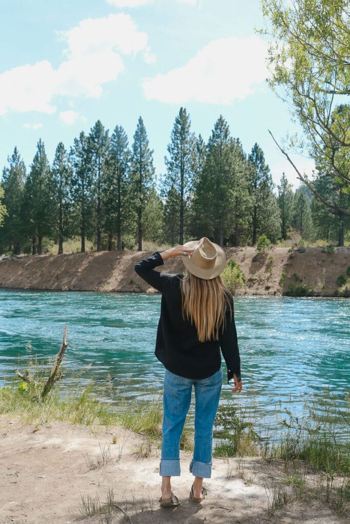 A woman stands looking at a turquoise river
