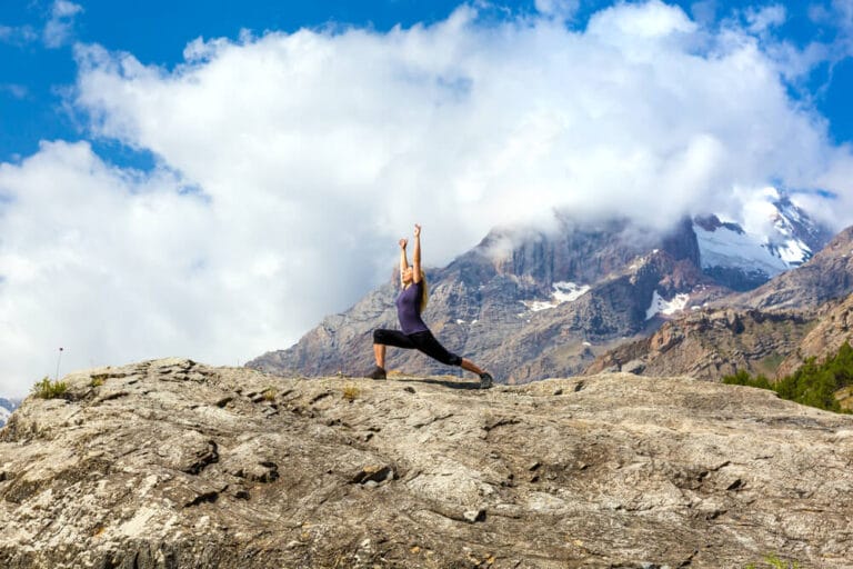 A woman in high lunge and arms stretched high atop a mountain