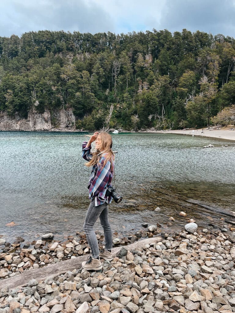 A woman stands on a rocky beach by a teal lake in Argentina