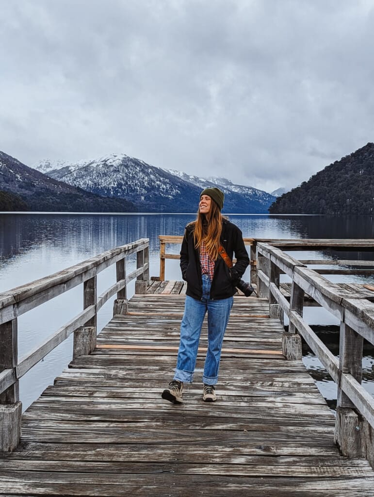 A woman stands on a wooden pier on a deep blue lake in winter