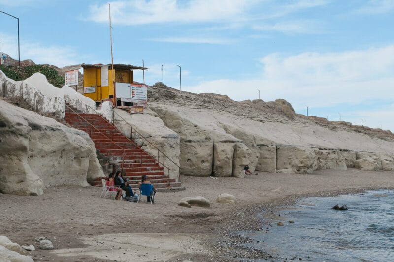 Three people sit in folding lawn chairs on the beach by the cliffs in Las Grutas Argentina