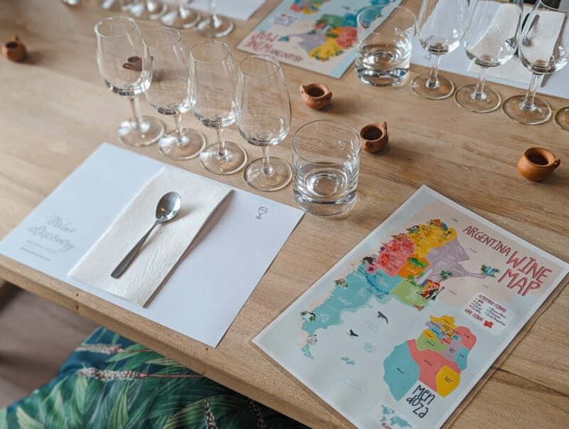 A colorful map of Argentina displays wine regions next to four empty wine glasses and a placemat on a table