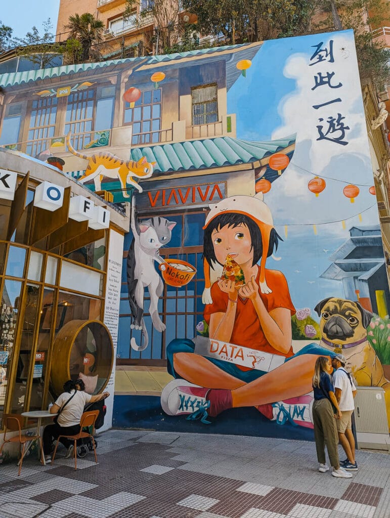 A mural of a little girl eating a slice of pizza with cats hanging down around her in Barrio Chino Buenos Aires