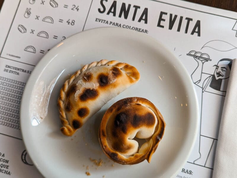 Two empanadas on a white plate with a Santa Evita place mat underneath