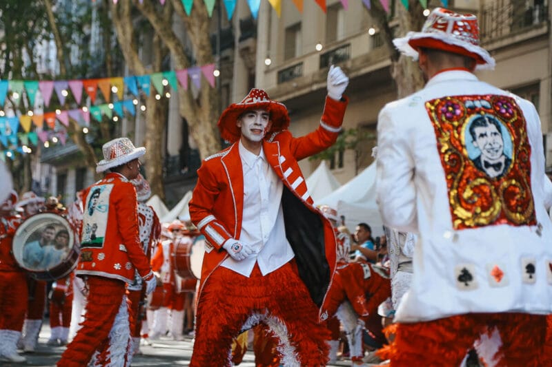 A parade of men dressed in red and white suits with glitter and tassles dance and play the drums for Carnival in Buenos Aires