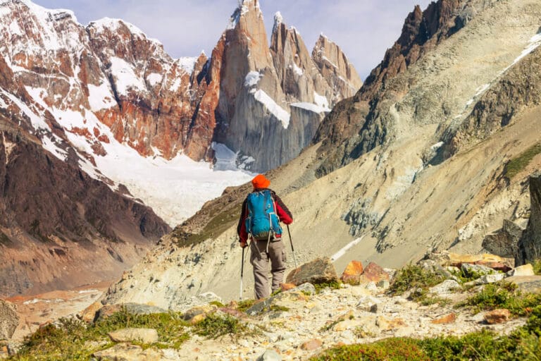 A man hikes with hiking poles and blue backpack towards the Laguna Torre mountains in El Chalten