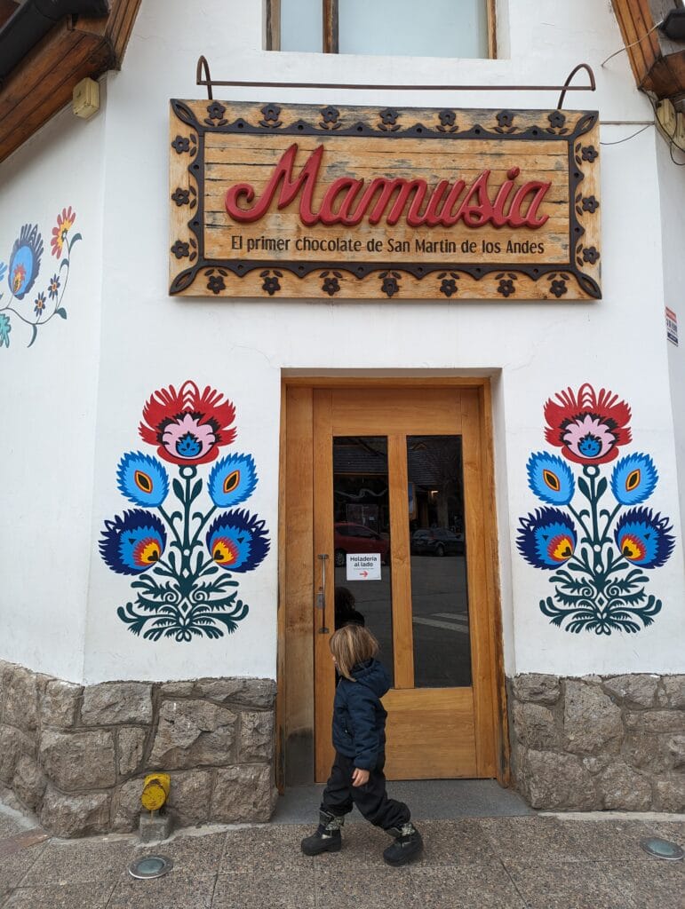 A small boy walks in front of the door of a white corner building decorated with flowers