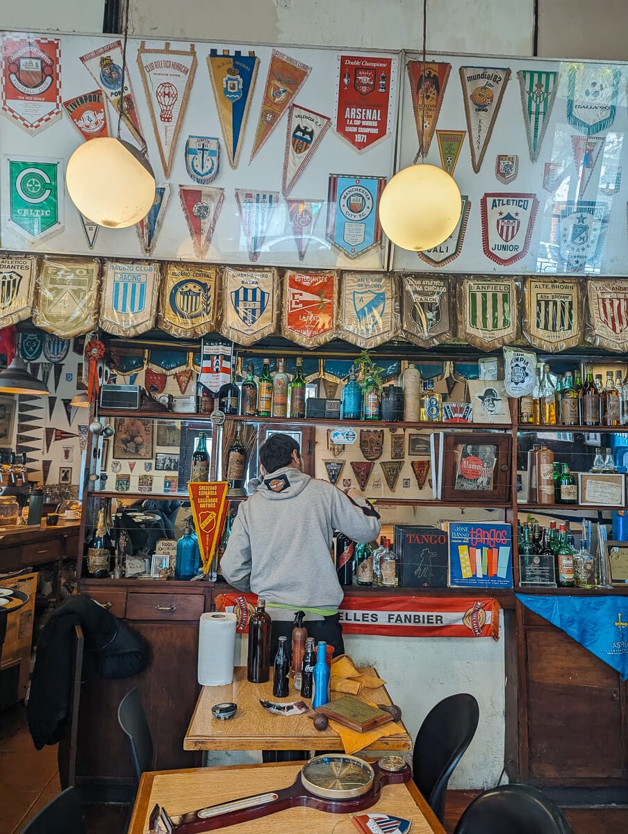 A man stands at a bar covered in football flats overhead and behind the bar
