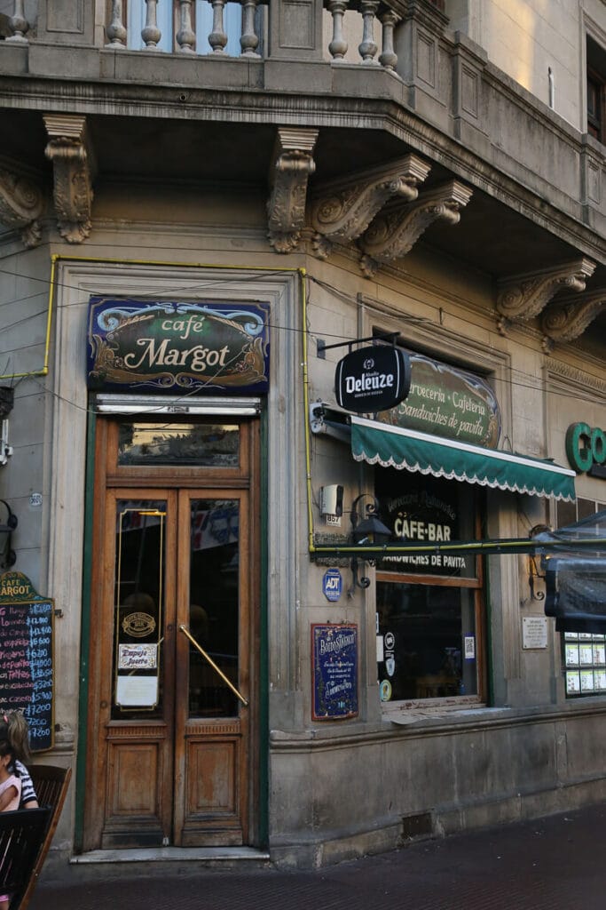 The exterior of a historic bar notable in Buenos Aires shows a wooden double door entrance and fileteado painted signs over the door and windows